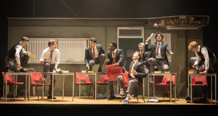 The boys from The History Boys dance in front of a classroom set.