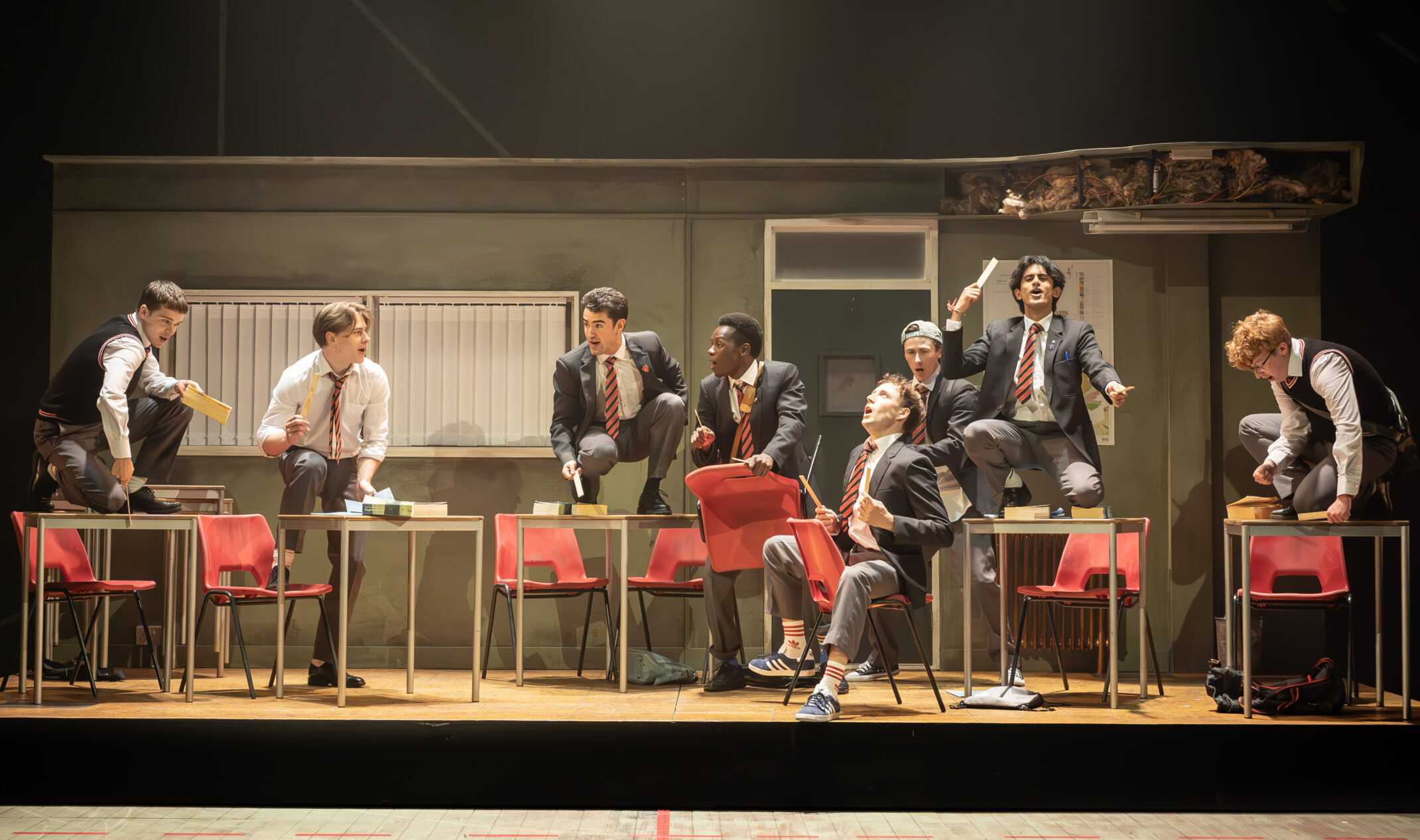 The boys from The History Boys dance in front of a classroom set.